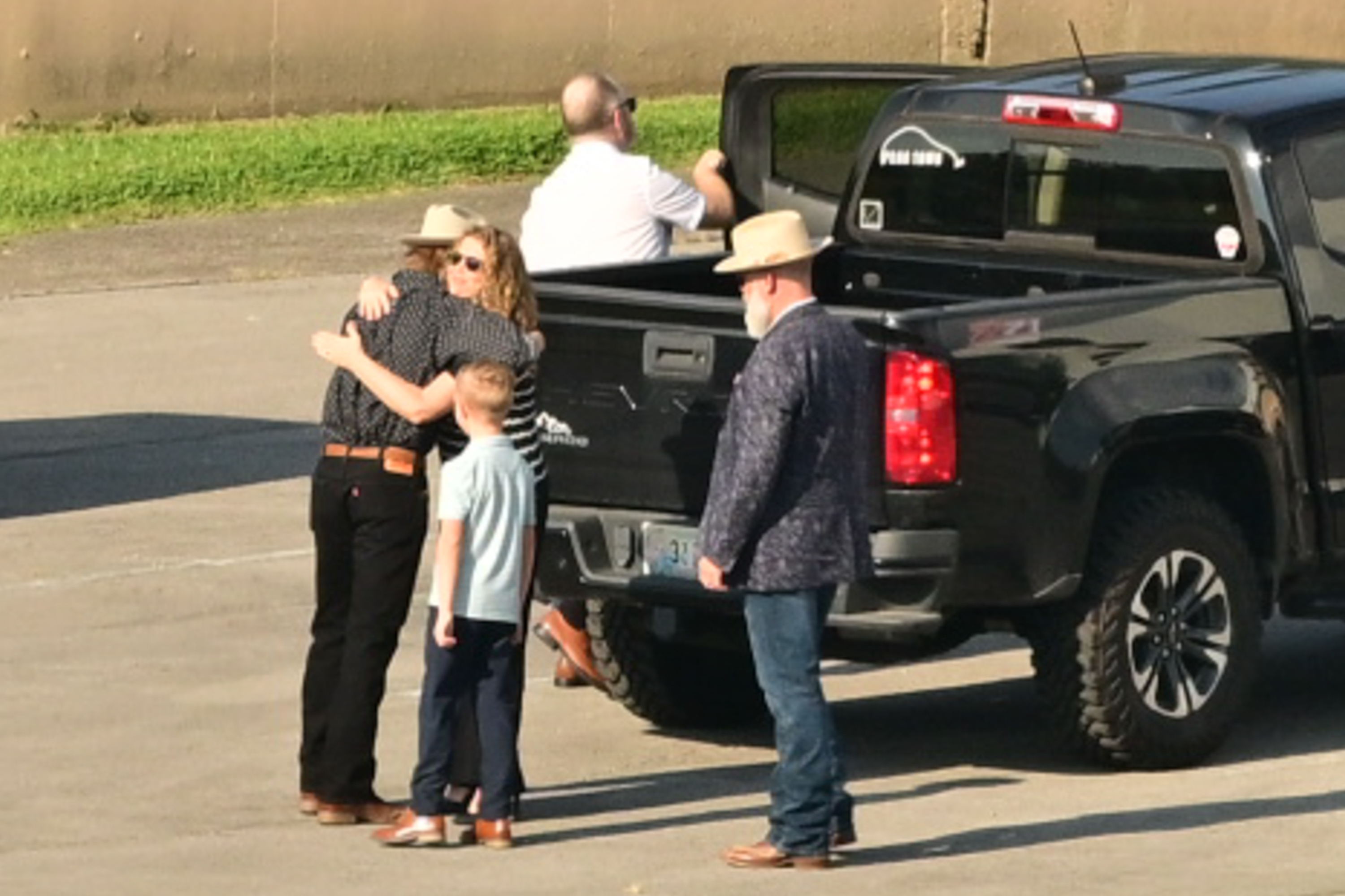 A group of people embracing near a black pickup truck.
