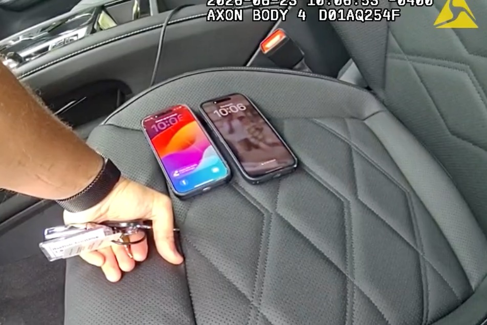 A body camera footage showing a person's arm and hand holding car keys, with two cell phones lying on a car seat.