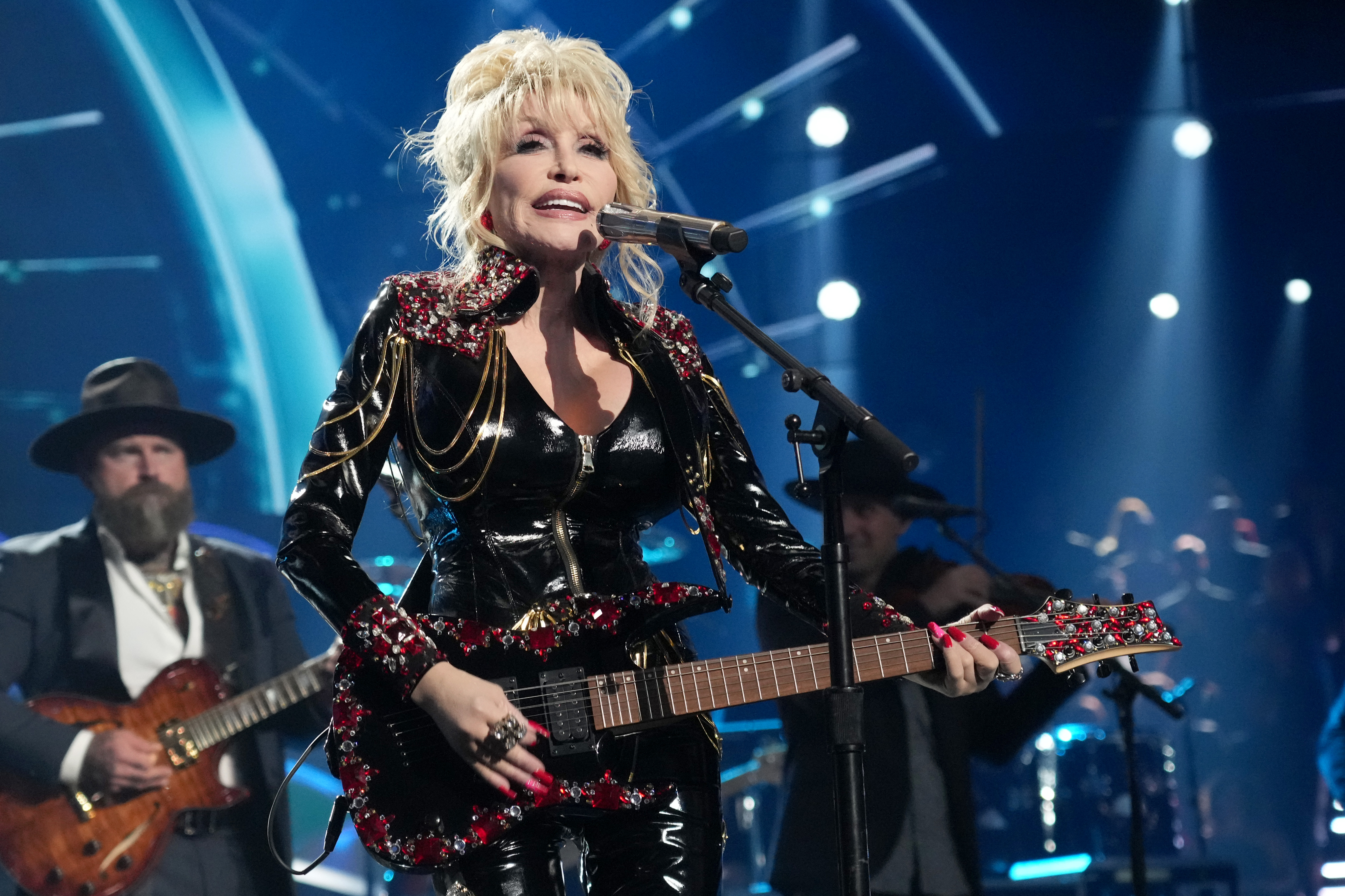 Dolly Parton performing live, holding an electric guitar and singing into a microphone.