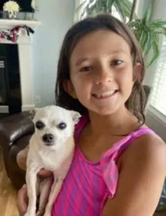 Mya Golabek, a smiling young girl in a pink swimsuit, holding a small white dog.